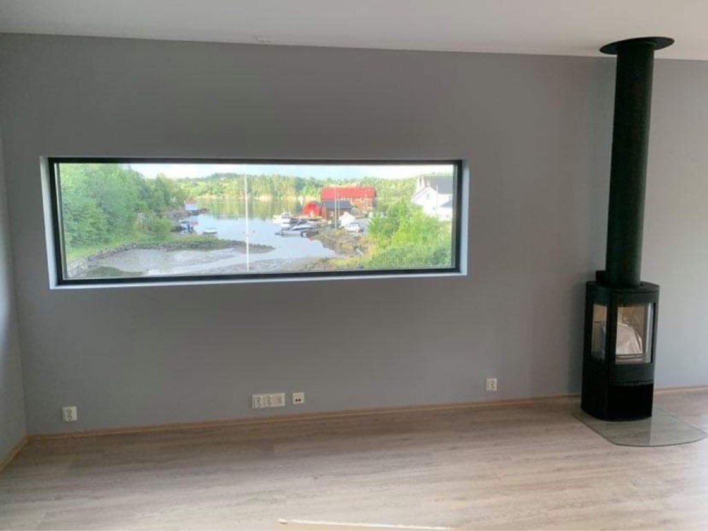 Stue med vedovn og panoramavindu mot vannet