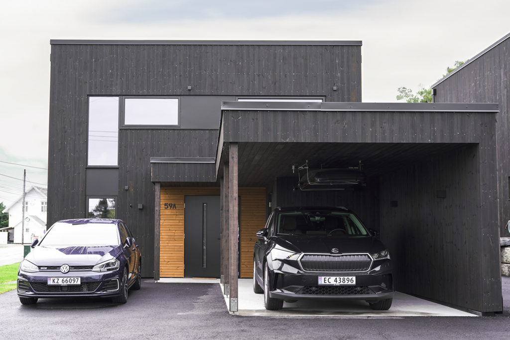 Mørkt hus med overbygd biloppstilling og to biler