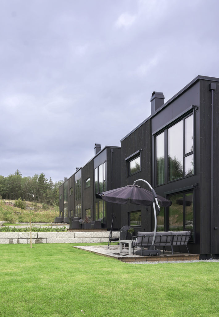 Rekke med mørke hus og terrasser langs en plen